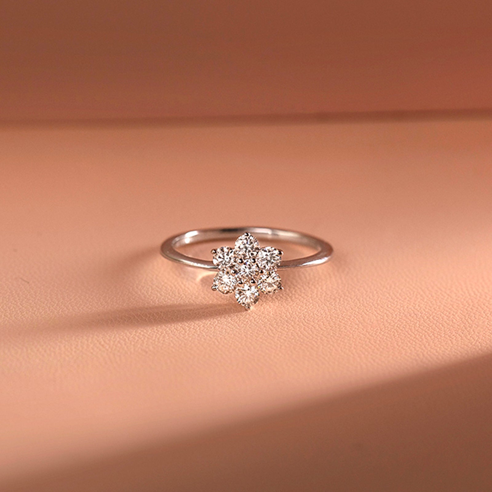 White Gold Engagement Diamond Ring with a diamond flower setting on a peach-colored fabric background