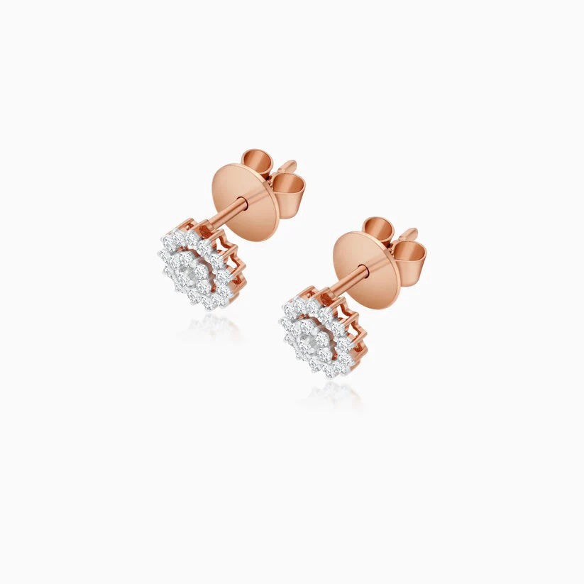 A pair of rose gold stud earrings with clear gemstones, shown from a three-quarter angle on a light gray background.