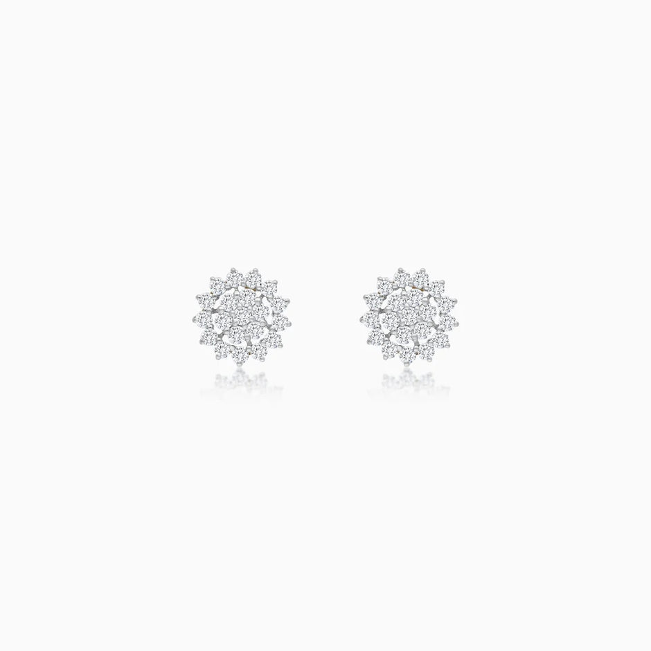 A pair of white  stud earrings with intricate, multi-layered snowflake or starburst designs set with clear diamonds, displayed on a clean white background with a soft reflection below.